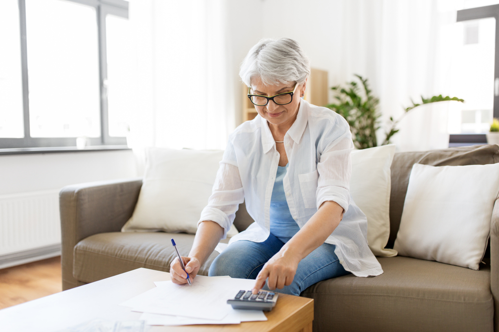 Senior woman filling out paperwork and using a calculator