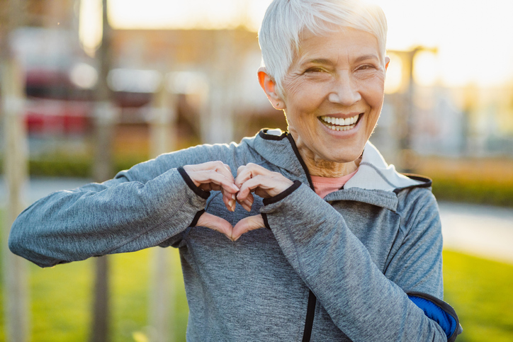 Portrait of smiling senior woman with short hair in sports clothing making a heart sign with her hands.