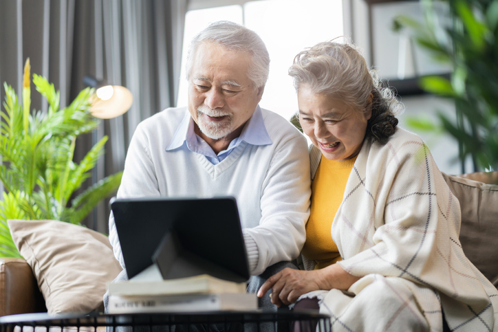 Senior couple sitting on a sofa in front of a computer with smiles on their faces.