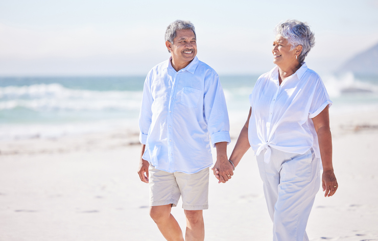 A senior man and a senior woman walking on a beach and holding hands
