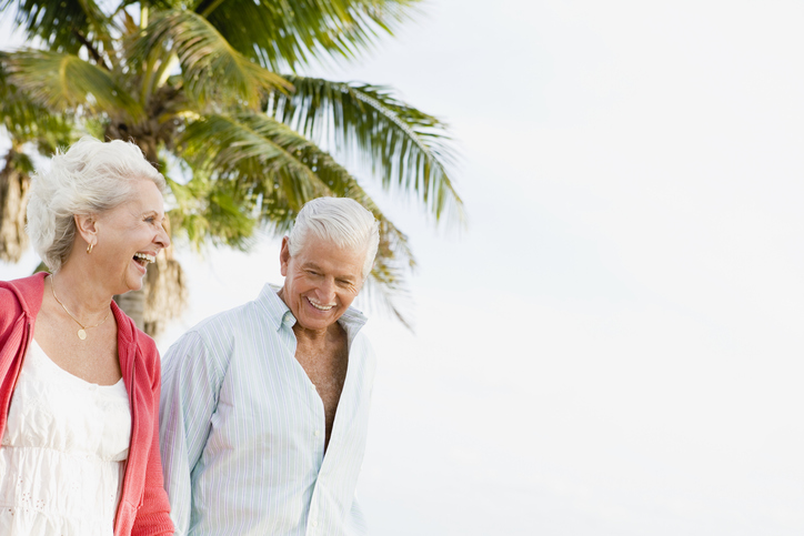 Senior man and woman smiling in front of a palm tree.
