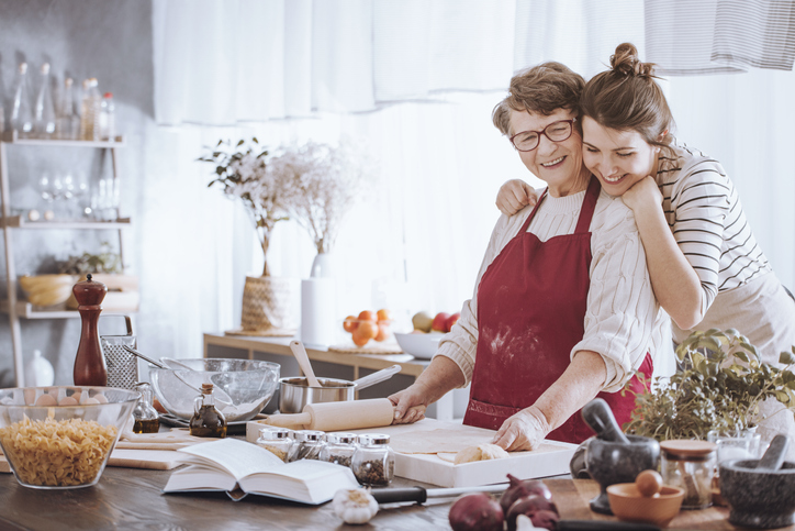 Granddaughter hugging grandmother while making cake together in the kitchen.