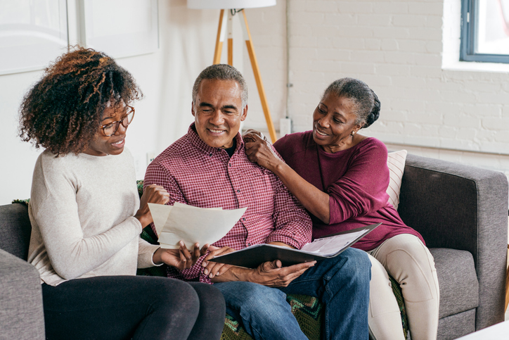 adult daughter sitting with older adult parents on couch and reviewing documents