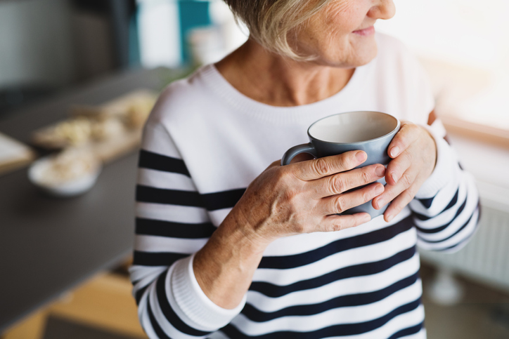 Older adult woman holding cup of tea in kitchen.